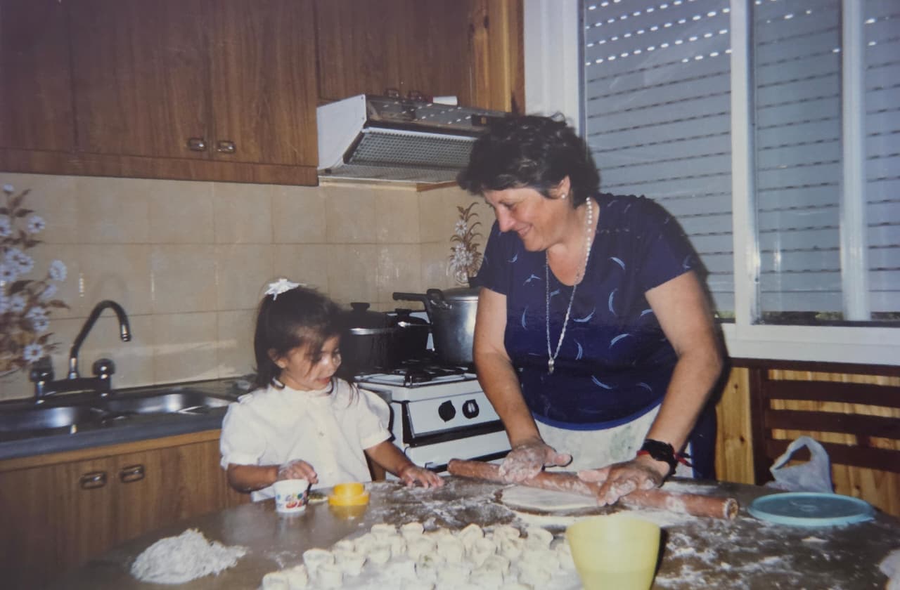Una niña junto a su abuela preparando masa en la cocina familiar